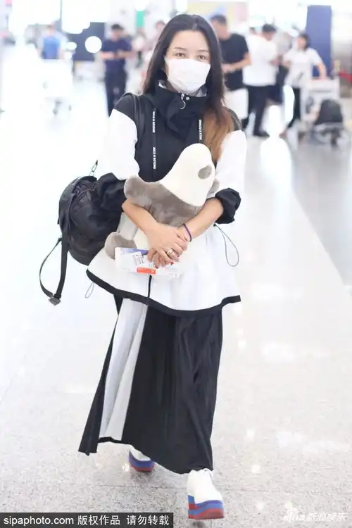 组图何洁着黑白长裙套装现身机场戴口罩怀抱公仔行色匆匆